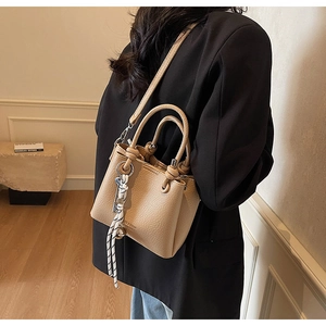 Détail du sac seau en cuir grainé beige avec poignées nouées et breloque rayée
