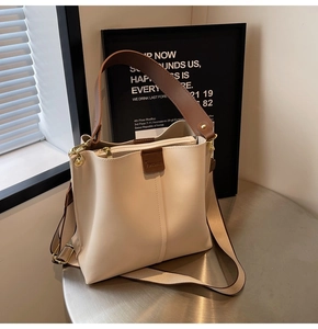 Close-up of cream bucket bag with brown wide handle and khaki fabric shoulder strap