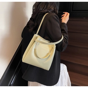 Creamy yellow bucket bag with metal ring handle shown on a model in a minimal setting