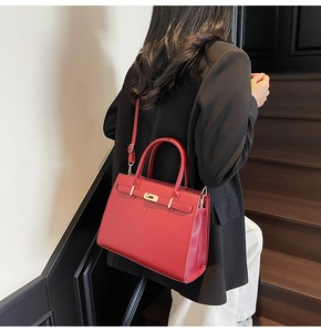 Modern red bridal handbag with golden twist lock detail shown on a wooden staircase