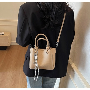 Détail du sac seau beige texture litchi avec breloque tissée sur veste noire