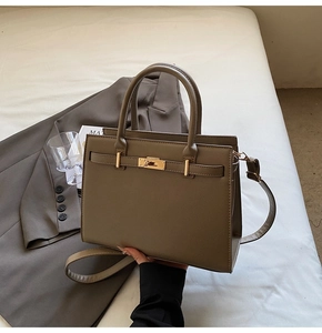 Detail of coffee brown structured leather handbag with gold metal clasp on white bedding