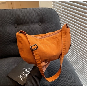 Detail of orange nylon crescent bag on grey corduroy sofa with adjustable strap and zipper