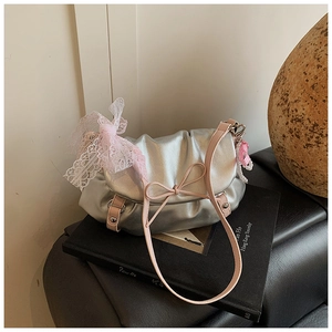 Détail d'un sac argenté métallisé avec bandoulière rose, nœud en dentelle et chaîne perle