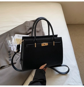 Macro detail of black textured leather bag with gold twist lock on white bedding