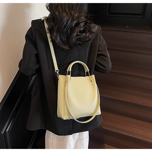 Detail of light yellow bucket bag with gold hardware worn by a model in black blazer