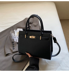 Detail of black cross-grain leather handbag with gold buckle and adjustable strap