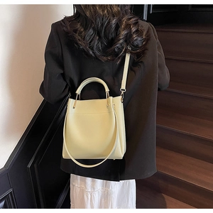 Minimalist creamy yellow leather bucket bag worn over the shoulder by a fashion model