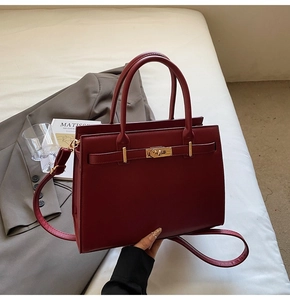 Detail of burgundy cross-grain leather handbag featuring golden twist lock and belt