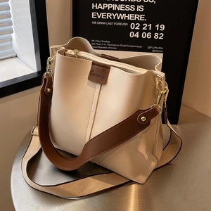 Chic beige bucket bag with brown wide strap on a silver table for daily commute
