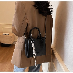 Détail du sac seau en cuir noir avec foulard rayé et pendentif argenté élégant