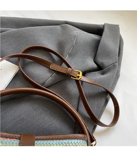 Close-up of brown leather shoulder strap and golden metal buckle on a woven bucket bag