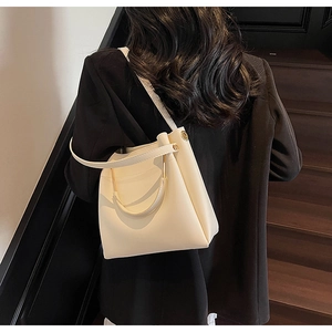 Detail of minimalist cream bucket bag with gold ring hardware on a black blazer