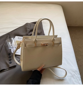 Detailed view of off-white faux leather tote bag with gold twist lock on white bedding