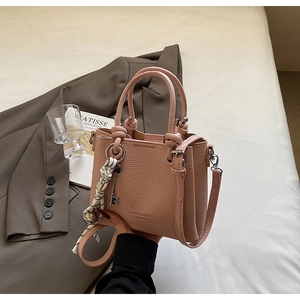 Gros plan d'un sac seau rose avec texture cuir et détail ruban sur tissu clair