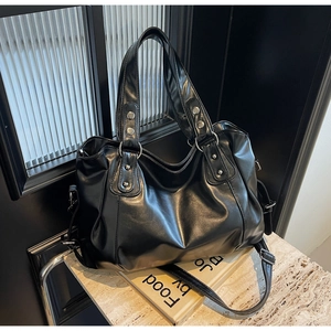 Detailed macro view of the black leather tote bag showing shiny texture and metal rivets