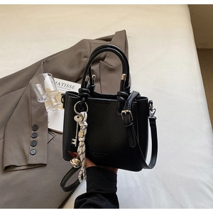Détail du sac seau en cuir noir avec foulard tressé et breloque en forme de clé