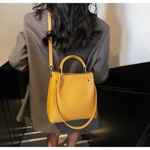 Minimalist ginger yellow bucket bag with metal handle shown on a grey suit model
