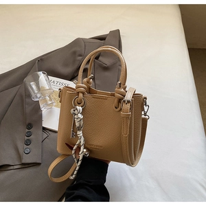Détail du sac seau en cuir camel avec poignée à nœud et lettrage doré sur fond beige