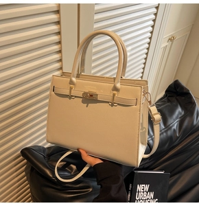 Detail of beige textured leather handbag with gold metal lock and adjustable shoulder strap