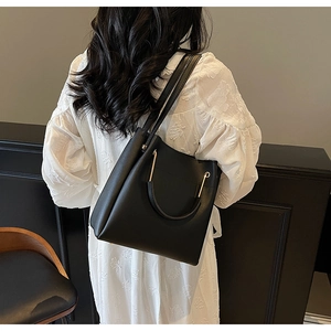 Detail of minimalist black tote bag featuring a round metal handle and slim shoulder strap