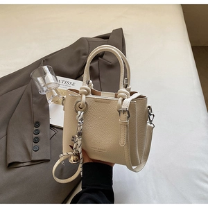 Détail du sac à main en cuir grainé crème avec nœud tressé et pendentif clochette