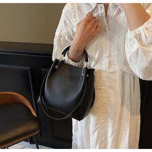 Detail of elegant black bucket bag with gold handle buckles worn by model in white dress