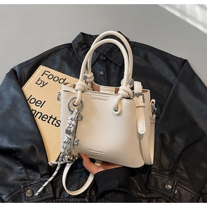 Détail du sac seau en cuir litchi blanc avec poignées à nœuds et accessoires charms