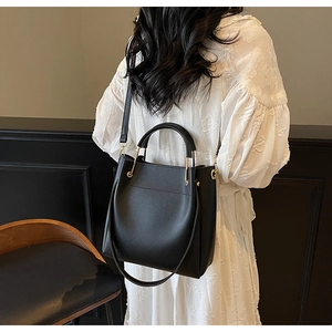 Detail of minimalist black leather bucket bag with metal handle worn on white textured dress
