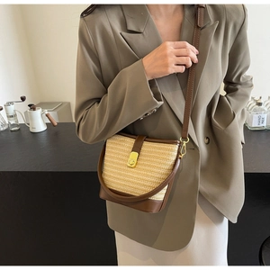 Detail of hand-woven straw bucket bag with brown leather trim and golden metal turn lock