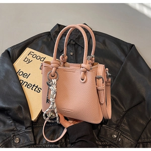 Détail d'un sac seau rose en cuir grainé avec breloques sur fond en cuir noir