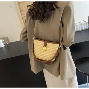 Detail of hand-woven straw bucket bag with brown leather trim and golden metal clasp