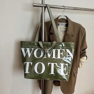 Dettaglio della borsa tote verde con scritte bianche e trama stropicciata su una gruccia