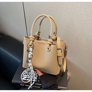 Détail du sac seau en cuir beige grainé avec décor argenté et poignée à nœud élégante