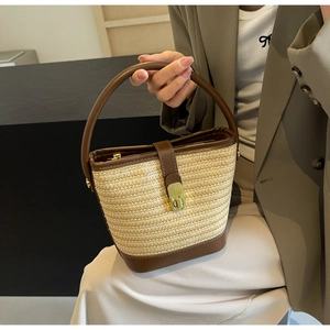 Detailed view of straw bucket bag featuring contrast leather trim and gold twist lock