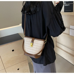 Detail view of woven straw bucket bag with brown leather trim and golden metal clasp lock