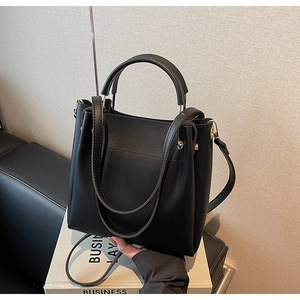 Detail view of matte black leather handbag with gold-tone hardware and adjustable strap