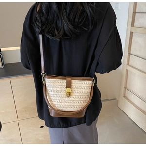 Detailed view of straw bucket bag with brown leather base and gold metal clasp closure