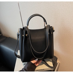 Detail of black matte leather bucket bag with gold hardware and dual cylindrical handles