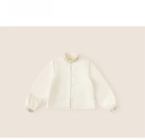 Detailed close-up of floral embroidery and pearl buttons on off-white kids oriental shirt