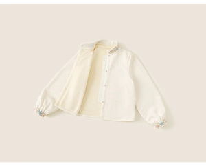 Detailed view of floral embroidery and pearl buttons on cream Chinese style kids shirt