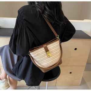 Detailed view of beige woven bucket bag featuring brown leather trim and golden metal clasp