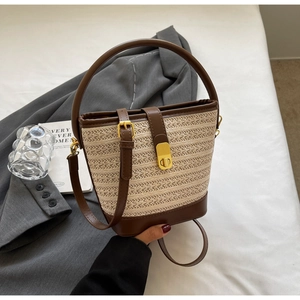 Detailed view of straw bucket bag featuring a large circular handle and golden turn-lock