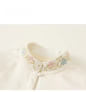 Detailed close-up of embroidered stand collar and pearl button on white girl shirt