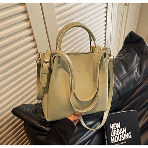 Detail view of sage green leather bucket bag with gold hardware in a modern indoor setting