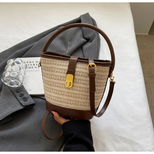 Detail of hand-held straw bucket bag with brown leather trim and golden lock