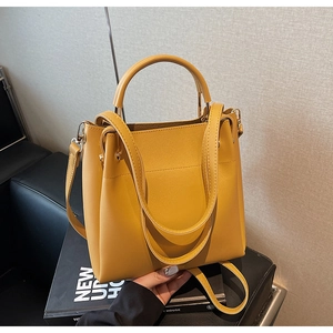 Detail of a ginger yellow leather bucket bag with top handle and metal side buckles