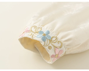 Close-up of floral embroidery and gold thread details on the off-white velvet sleeve