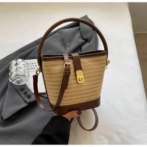 Detail view of woven straw bucket bag with dark brown leather handle and gold twist lock