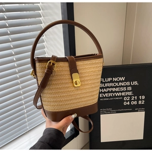 Close-up of woven straw bucket bag featuring brown leather trim and golden metal twist lock